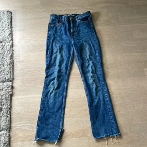 Blå raka jeans från Zara, strl 34 - Snygga blå jeans från Zara i rak modell med hög midja. Jeansen har klassisk femficksdesign, råa och fransiga benslut samt dragkedja och knapp framtill. Perfekta för en avslappnad och trendig look. Ser bättre ut(inte lika skrynkligt) på, skriv om du vill ha bilder med de på.