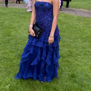 Blå axelbandslös balklänning - En fantastisk blå axelbandslös balklänning med vackra broderier och pärlor upptill. Klänningen har en lång, volangig kjol i flera lager som ger en riktigt drömmig känsla. Enormt unik och i superfint skick!