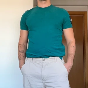 Turkos t-shirt från North Face - Säljer en turkos t-shirt från The North Face med logga på ärmen och ryggen. T-shirten är i klassisk modell med rund hals och korta ärmar. Skön passform och tillverkad i mjuk bomull, perfekt för en chill och stilren look. Den har en fläck på framsidan vid vänstra bröstet, inget som märks vid användning. 