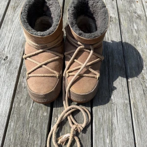 Beiga/bruna Inuikii moon boots i mocka - Säljer ett par beiga Inuikii moon boots med mjukt foder och grov snörning. Skorna är i mocka med ullfoder och har en rejäl sula som ger bra grepp. Perfekta för kalla dagar och har en riktigt mysig vibe.