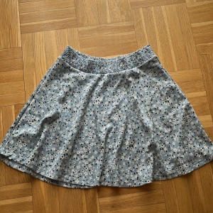 Blommig blå kjol  - Supersöt kortkjol i ljusblå med små vita och svarta blommor. Kjolen har resår i midjan