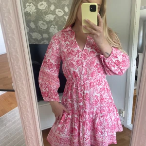 Zara klänning - Supersöt kortklänning i rosa och vitt med härligt mönster och volangkant. Klänningen har långa ärmar, markerad midja och v-ringning. Perfekt för sommarens alla tillfällen ☀️