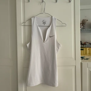 Vit Dri-Fit linnetopp från Nike XS - Säljer en vit sportig linnetopp från Nike i Dri-Fit-material. Toppen har djup v-ringning, brottarrygg och är ärmlös. Perfekt för träning eller när du vill ha en luftig och bekväm look. Nike-logga framtill för extra sportig vibe.