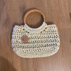 Handgjord beige handväska med trähandtag - Superfin handgjord handväska i beige med grovt stickat mönster och runda trähandtag. Perfekt accessoar för dig som gillar en bohemisk och unik stil. Väskan är rymlig och passar till många olika outfits.