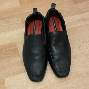 Svarta loafers i skinn  - Stilrena svarta läder loafers med fyrkantig tå och låg klack. Skorna är gjorda i mjukt skinn och har en röd innersula. Storlek 36 med 3cm klack. Har använt de ett fåtal gånger. 