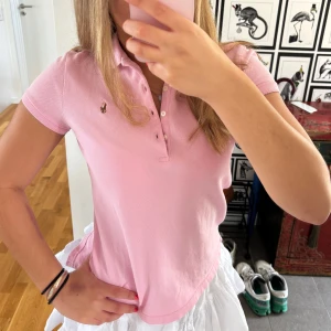 Rosa tröja från Polo Ralph Lauren - Supersöt rosa tröja från Ralph Lauren med krage, knappar och klassisk broderad logga. Tröjan är i mjuk bomull och har korta ärmar💞storlek 16år (XS)