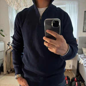 Marinblå stickad half zip från Hampton Republic - Snygg marinblå stickad tröja från Hampton Republic med half zip-dragkedja och hög krage. Tröjan är ribbstickad och har lång ärm, perfekt för lager-på-lager. Passar dig som gillar klassisk och clean stil.
