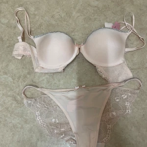Ljusrosa spets-bh från Hunkemöller - Supersöt ljusrosa bh från Hunkemöller med glittriga detaljer längs kanten och tunna axelband. Bh:n har spets på sidorna och en liten rosett framtill. Matchande trosor i samma färg med spets och små hjärtan. Perfekt för dig som gillar romantiska vibes.