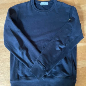 Mörkblå Stone Island sweatshirt - Snygg mörkblå sweatshirt från Stone Island med klassisk rund hals och ikonisk patch på vänster ärm. Tröjan är i mjuk bomull och har ribbade muddar vid ärmslut och midja. Perfekt för dig som gillar streetwear och vill ha en clean look.Nypris på denna tröja är 3000kr men är ändå mycket villig att förhandla 