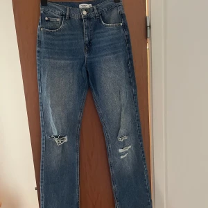 Blå slitna jeans från Pull&Bear - Snygga blå jeans från Pull&Bear med slitningar på knäna och bakfickan. Modellen har raka ben med slits vid anklarna
