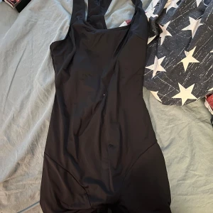 Svart baddräkt med breda axelband - Enkel och stilren svart baddräkt med breda axelband och klassisk skärning. Perfekt för simning eller strandhäng. Sitter tight och har en sportig look som passar dig som gillar minimalistisk stil. Helt oanvänd 