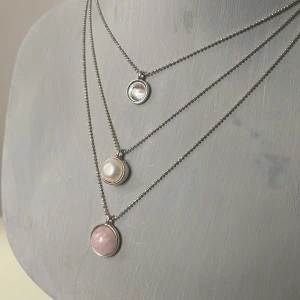 Set med halsband och armband från lbvyr - Snyggt set från lbvyr med tre lager halsband och matchande armband i silverfärgad metall. Båda har runda hängen med en klar sten, en vit pärla och en ljusrosa sten. Kedjorna är tunna och stilrena, perfekt för att ge din look lite extra shine.