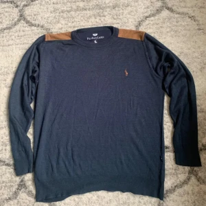 Två långärmade tröjor från Polo Ralph Lauren - Säljer två snygga långärmade tröjor från Polo Ralph Lauren. En är marinblå med bruna axelpartier och broderad logga, den andra är turkos med matchande broderad logga. Båda har rund hals och är i mjuk bomull, perfekta för lager-på-lager under höst och vår.