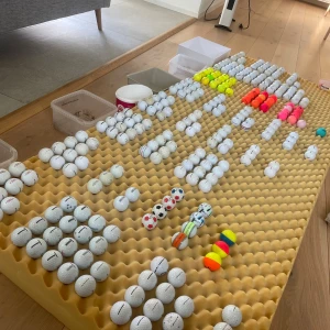 300+ golf bollar  - Bilden visar ett stort antal golfbollar i olika färger och mönster, noggrant sorterade på en skumgummimadrass. Perfekt för dig som älskar golf och vill ha många bollar att träna med eller samla på. Här finns både klassiska vita och färgglada varianter – redo för nästa runda!