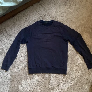 Mörkblå sweatshirt från Emporio Armani - Snygg mörkblå sweatshirt från Emporio Armani med diskret logga på bröstet. Tröjan har rund hals, långa ärmar och ribbade muddar vid ärmslut och nederkant. Perfekt för dig som gillar stilrena och klassiska plagg med exklusiv känsla.