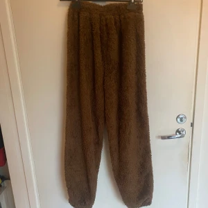 Bruna fluffiga mjukisbyxor - Supermysiga bruna mjukisbyxor med fluffig yta och avslappnad passform. Perfekta för chill hemma eller när du vill vara extra bekväm. Resår i midjan och vid bensluten för skön känsla. Materialet är fleece som känns mjukt mot huden.