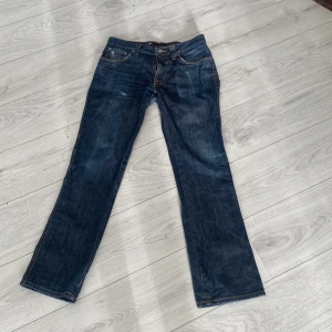 Mörkblå jeans från Nudie Jeans W31 L32 - Snygga mörkblå jeans från Nudie Jeans med klassisk femficksdesign och kontrastsömmar. Modellen har raka ben och coola broderade detaljer på bakfickorna. Perfekt passform för dig som gillar en tidlös och clean look. Materialet är slitstarkt denim i bomull.