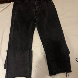 Svarta raka jeans med rå kant - Svarta jeans med rak passform och rå, ofållad kant längst ner på benen för en edgy vibe. Jeansen har klassisk femficksdesign och är tillverkade i jeansmaterial. Perfekt för dig som gillar en enkel men cool stil.