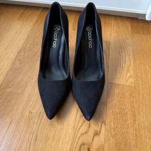 Pumps med låg stilettklack  - Säljer ett par stilrena svarta pumps från Boohoo i storlek 39. Skorna har spetsig tå och hög klack, vilket ger en snygg och elegant look. Materialet är mocka. Använt enstaka gånger.