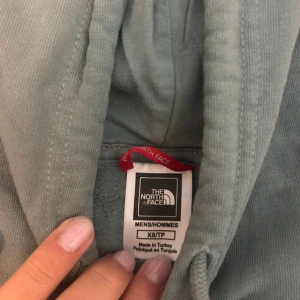 Grå hoodie från The North Face XS - Säljer en grå hoodie från The North Face i storlek XS. Tröjan har stor vit logga framtill, huva med snörning och en klassisk magficka. Mjuk insida och ribbade muddar vid ärmslut och nederkant. Perfekt för chill dagar eller när du vill ha en clean streetstyle.