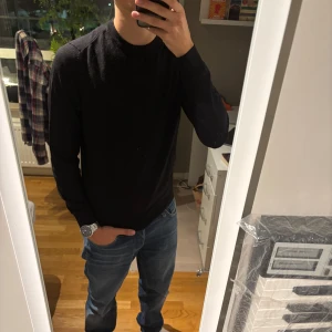 Svart stickad tröja med rund hals - Snygg svart stickad tröja med rund hals och lång ärm. Enkel och stilren design som passar perfekt till jeans. Tröjan har en normal passform och är tillverkad i ett mjukt stickat material som känns skönt mot huden.