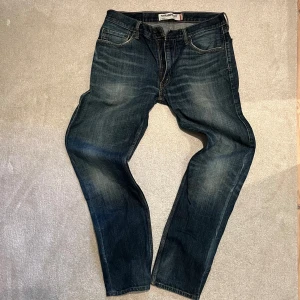 Levi's 505 straight fit jeans blå - Säljer ett par Levi's 505 straight fit jeans i klassisk mörkblå tvätt med snygga slitningar. Modellen har fem fickor, dragkedja och knappstängning. Jeansen har normal passform och raka ben, perfekt för en chill och stilren look. Lite slitna vid hälen men tycker bara det blir snyggare!!