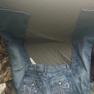 Blå bootcut jeans med rosett-detalj - Snygga blå jeans från gina tricot  i bootcut-modell med coola rosettbroderier och nitar på bakfickorna. Jeansen har normal passform, klassisk femficksdesign och är gjorda i mjukt denimtyg. Perfekt för dig som vill ha en unik look med extra detaljer.