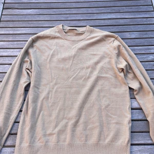 Beige  fin stickad tröja med rund hals - Säljer en enkel och stilren beige stickad tröja med rund hals. Tröjan har långa ärmar och ribbade muddar vid hals, ärmslut och nederkant. Perfekt för lager-på-lager och passar till jeans eller chinos.