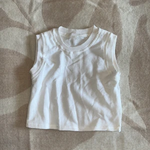 Vit ärmlös linnetopp - En enkel och clean vit linnetopp med rund hals och ärmlös design. Toppen är gjord i mjuk bomull och har en rak passform som sitter snyggt på kroppen. Perfekt att styla med jeans eller shorts för en chill look.