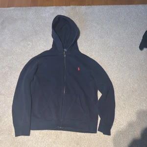 Mörkblå zip hoodie från Polo Ralph Lauren - Säljer en mörkblå hoodie från Polo Ralph Lauren med röd logobroderi på bröstet. Vid snabb affär kan priset förhandlas!