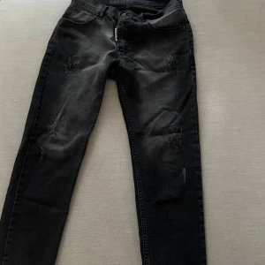 Svarta Dsquared2 ICON jeans - Snygga svarta jeans från Dsquared2 ICON-kollektionen med coola slitningar och tvättad look. Modellen har klassisk femficksdesign, knapp med Dsquared2-logga och patch med Zlatan Ibrahimovic-citat bak. Passar dig som gillar streetstyle och exklusiva märken.