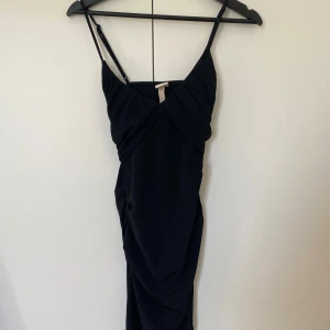 Svart midiklänning med slits från H&M -  svart klänning från H&M med smala axelband och draperad v-ringad överdel. Klänningen har en slits på sidan och är figurnära i passformen. 