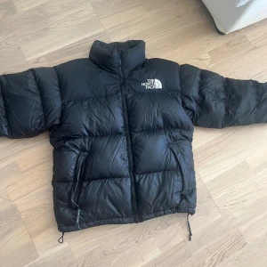 Svart dunjacka från The North Face S - Säljer en svart pufferjacka från The North Face i storlek S. Jackan är dunfylld, har hög krage, dragkedja framtill och två fickor med dragkedja. Klassisk logga broderad på bröstet. Perfekt för kalla dagar och riktigt snygg streetstil. En liten defekt som syns på bild 4a.