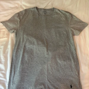Grå t-shirt från Polo Ralph Lauren - Snygg grå t-shirt från Polo Ralph Lauren med klassisk rund hals och korta ärmar. Tillverkad i mjuk bomull och har den ikoniska svarta Polo-loggan broderad längst ner. Perfekt basic för garderoben och enkel att matcha med allt. Fin och nästan aldrr använd