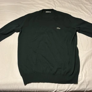 Mörkgrön stickad tröja från Lacoste - Snygg mörkgrön stickad tröja från Lacoste i klassisk passform. Använt en gång. Storlek L
