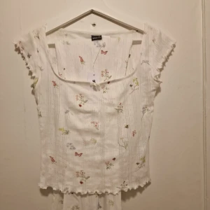 Vit blommig set från Gina Tricot - Supersöt vit topp och tillhörande byxor från Gina Tricot med små blommor och fjärilar i olika färger. Slutsålt och går ej att köpa längre, de är i pointelle material. 