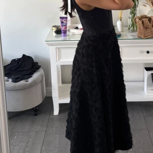 Svart långklänning med textur - Säljer en svart långklänning med ärmlös överdel och en kjol med cool textur som ger en unik look. Klänningen har en markerad midja och dragkedja i sidan. Perfekt för dig som vill sticka ut med en elegant och modern stil.  Helt ny med prislapp på Nypris 899kr . Storlek XS