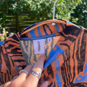 Mönstrad långärmad polotröja från Junkyard - Säljer en unik långärmad polotröja från Junkyard i storlek XS. Tröjan har ett coolt abstrakt mönster i orange, blått och svart med hög krage. Materialet är tunt och stretchigt, perfekt för dig som gillar statement-plagg :)