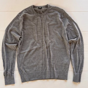 Grå merinoulltröja från Uniqlo - Säljer en stilren grå tröja från Uniqlo i mjuk merinoull. Klassisk rund hals och långärmad modell med ribbade muddar och nederkant. Perfekt för lager-på-lager och chill höst- och vinterdagar. Enkel att matcha med jeans eller chinos. 