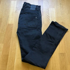 Replay Anbass svarta jeans, W29 L34 - Säljer ett par svarta Replay Anbass jeans i klassisk femficksmodell. Jeansen har smal passform, raka ben och snygga detaljer vid fickorna. Materialet är mjukt och stretchigt för extra komfort. Perfekta för dig som gillar stilrena och moderna jeans.