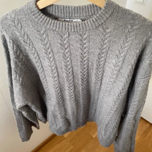 Grå stickad tröja från NA-KD - Säljer en grå stickad tröja från NA-KD i storlek XS. Tröjan har ett snyggt flätmönster, rund hals och långa ärmar. Den är loose fit och passar perfekt för dig som gillar chill och comfy vibes🩶