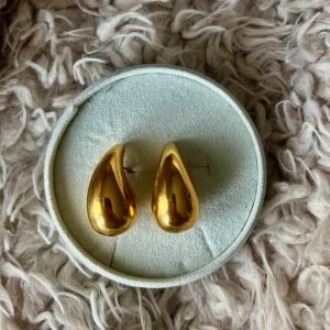 Droppformade guldörhängen - Stilrena guldfärgade örhängen i droppform. Aldrig använda, alltså i ny skick. Passar både till vardag och fest. Lätta och bekväma att bära.