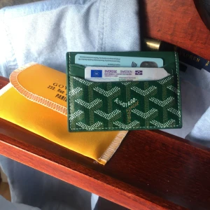 Grön goyaard plånbok med mönster  - Säljer en grön plånbok ikoniska vita och gröna mönster. Plånboken är tunn och smidig, perfekt för kort och sedlar. Kommer med gult fodral. Snygg accessoar för dig som gillar stil. Box följer ej med