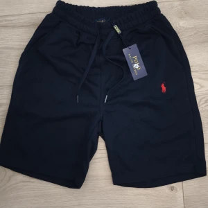 Marinblå shorts från Polo Ralph Lauren - Snygga marinblå shorts från Polo Ralph Lauren med röd broderad logga på benet. De har elastisk midja med snörning.                                                      📏Storlek: M                                                            💡Meddela för mer information eller frågor