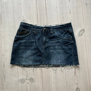 Blå lågmidjad jeanskjol  - Mörkblå fransad lågmidjad jeanskjol från Yessica i fint skick. Kan inte hitta storlek men skulle säga S/M. Tvärs över midjan är det 40 cm och den är ca 32-33 cm lång. Använd gärna köp nu!