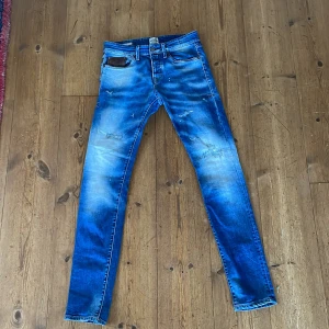 Blå slim fit jeans från Jack & Jones - Snygga blå jeans från Jack & Jones med slim fit passform. Modellen Glenn har slitna detaljer och en cool tvätt som ger en fräsch vibe. Klassiska fem fickor, läderpatch bak och smal siluett. Perfekta för dig som gillar en modern och stilren look.