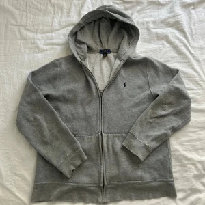 Grå hoodie från Polo Ralph Lauren XL - Säljer en grå hoodie från Polo Ralph Lauren i storlek XL. Tröjan har huva, dragkedja framtill och två fickor. Klassisk Polo-logga broderad på bröstet. Mjuk insida och långärmad modell, perfekt för chill dagar.