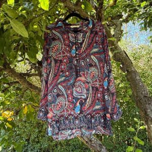 Mönstrad långärmad skjorta från Nelly - Färgstark långärmad skjorta från Odd Molly med paisley- och blommönster i blått, rött och beige. Skjortan har knappar framtill, klassisk krage och ett flowigt material som känns skönt mot huden. Perfekt för dig som gillar att sticka ut med coola prints. Storlek 3 som enligt deras storleksguide motsvarar en storlek L.  Mycket fint skick, jag hittar inga synliga anmärkningar eller defekter. 