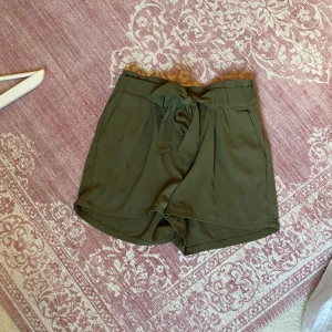 Olivgröna shorts med knytband - Snygga oliv/militärgröna shorts med hög midja och ett brett knytband framtill. De har en lös passform och är tillverkade i ett mjukt, lätt tyg., typ chiffong. 