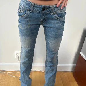 Lowwaist bootcut jeans från Hydraulic - As coola vintage blå jeans från Hydraulic med bootcut och låg midja. Jeansen har slitna detaljer, klassiska fem fickor och coola knappar på bakfickorna. 